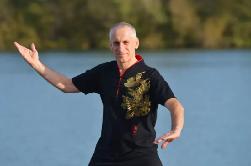 Laurent professeur de l’École des 3 énergies à Mâcon, vêtu d'une tenue traditionnelle chinoise noire avec une broderie de dragon doré et col rouge, enseignant de tai chi chuan et arts martiaux